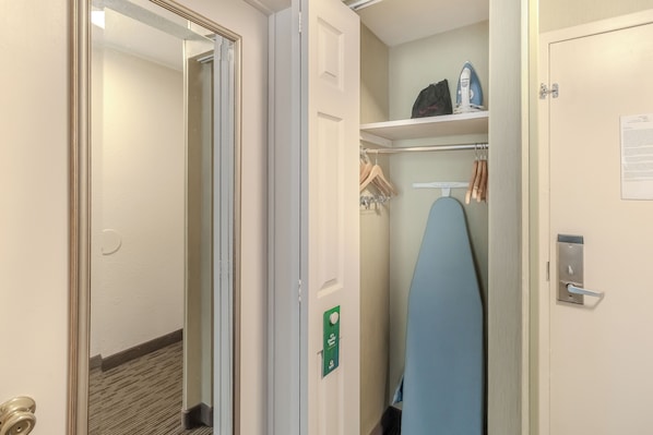 A hotel room with a door leading to a hallway, a coat rack with hangers, and a blue ironing board.