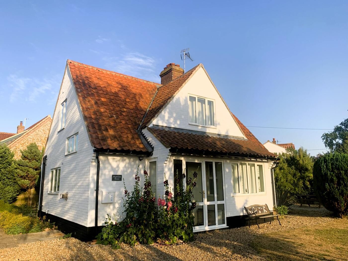 Een tweelaags huis met een schuine dak, schoorsteen en een veranda met een bank.