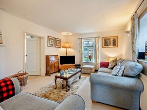 Ein Wohnzimmer mit Sofa, Fernseher, Lampe, einem Fenster mit Vorhängen und einer Tür.