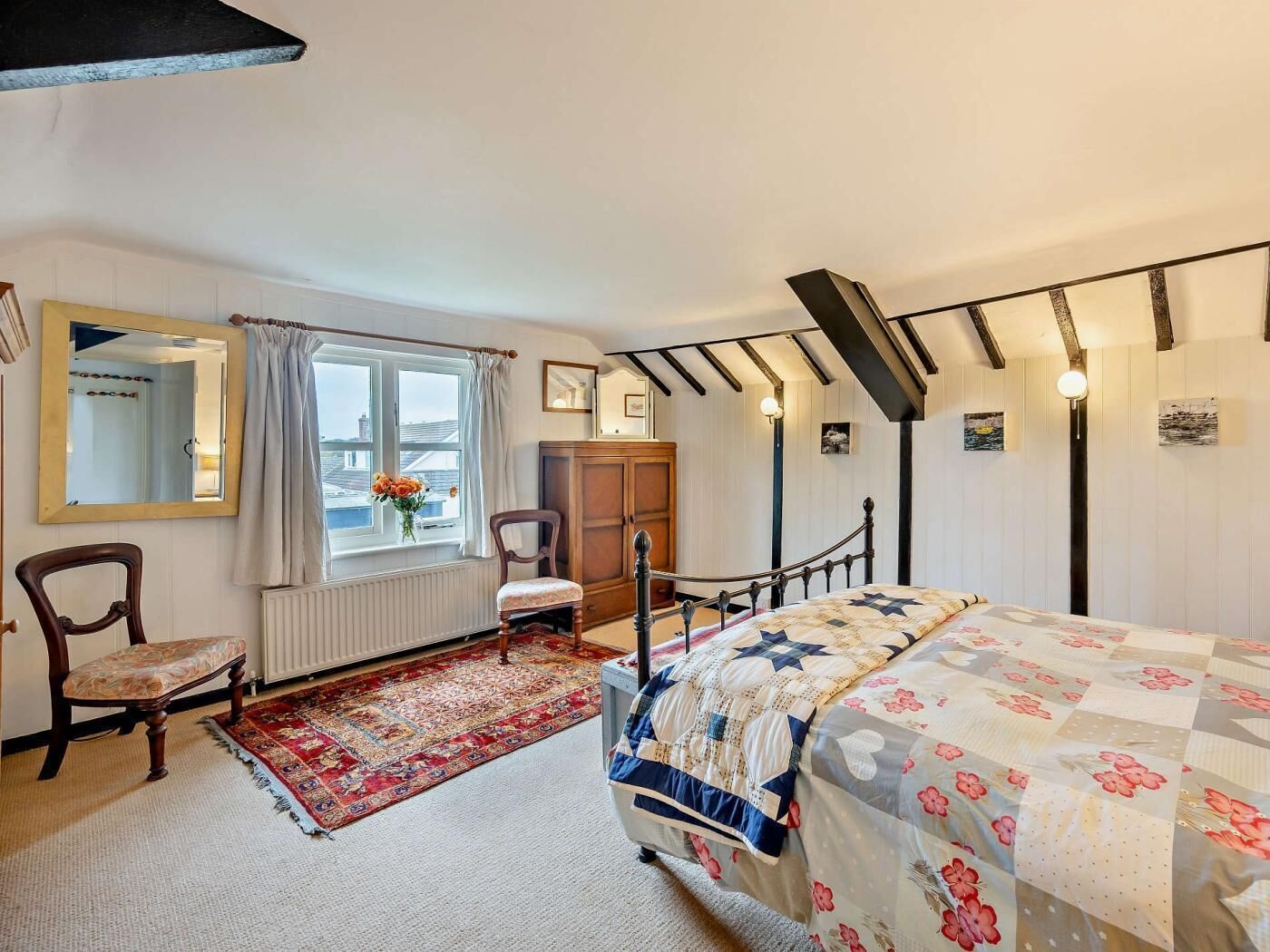 A bedroom with a bed, a chair, a dresser, a window with curtains, and a radiator.