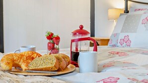 Ein Frühstücksbuffet mit Croissants, Erdbeeren, einer Kaffeekanne und einer Tasse auf einem Bett mit blumigem Bettzeug.