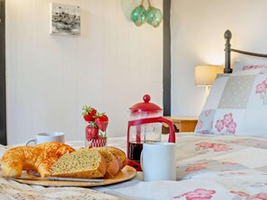 Ein Frühstücksbuffet mit Croissants, Erdbeeren, einer Kaffeekanne und einer Tasse auf einem Bett mit blumigem Bettzeug.