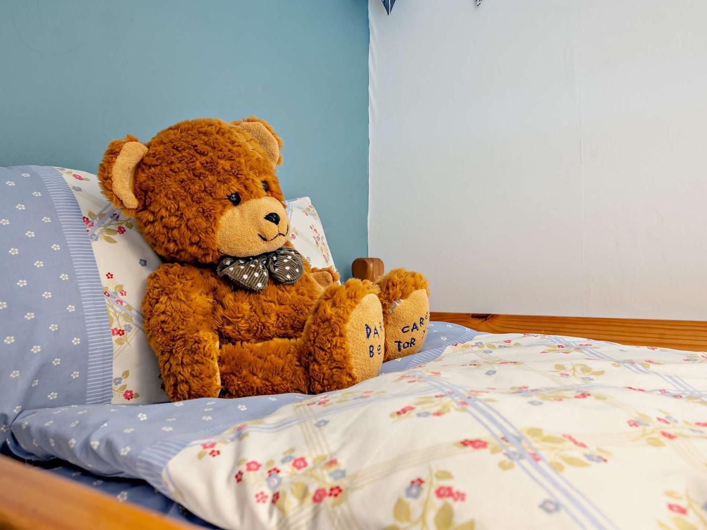 Ein Teddybär sitzt auf einem Bett mit Blumenmuster und einem blauen Kopfkissen.