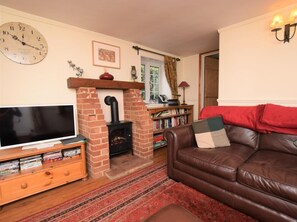 A living room with a television, a fireplace, a bookshelf, and a leather sofa. - 3 Bed in Syderstone (oc-kt083) (Syderstone)