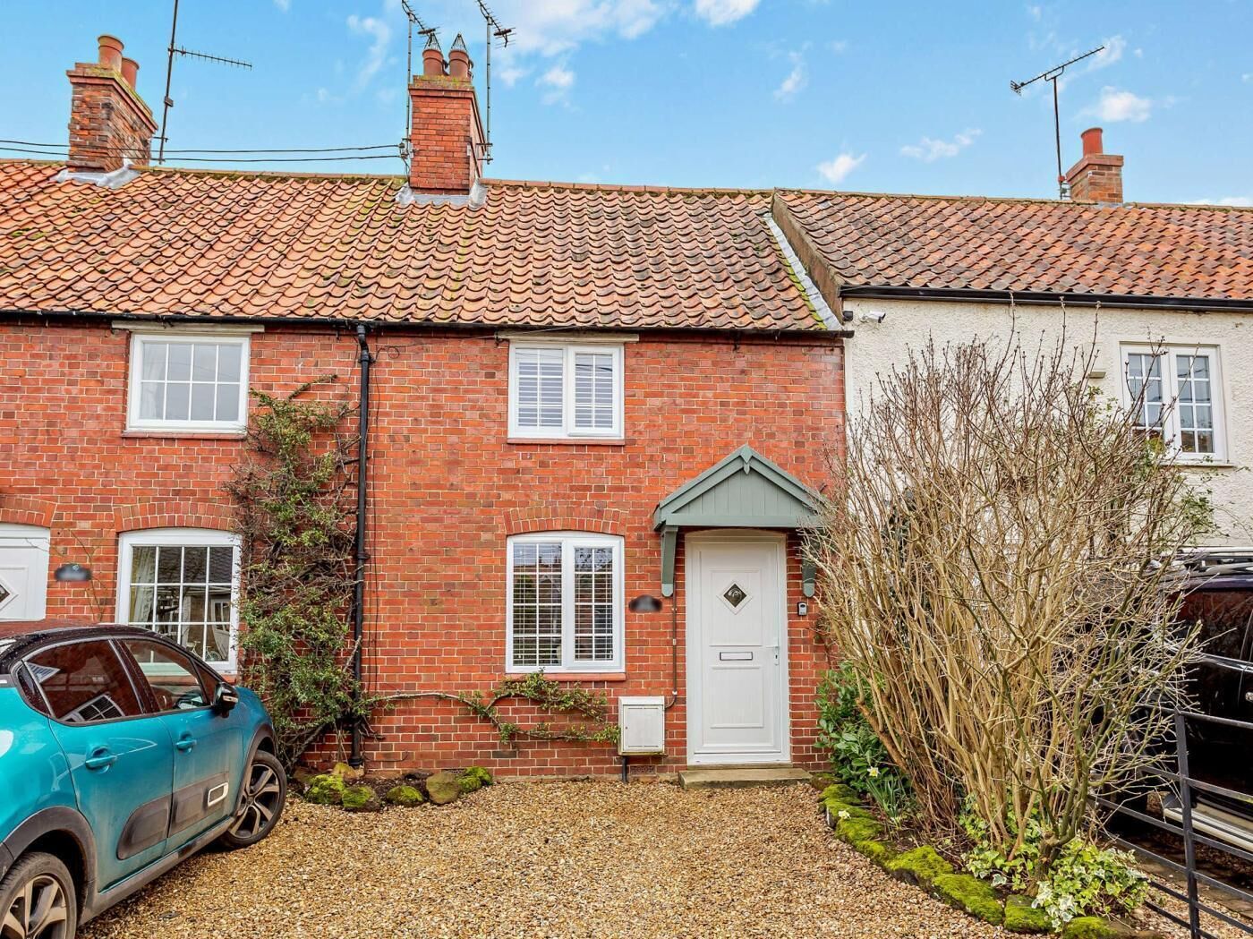 A brick house with a tiled roof, a white door, and a car parked in the driveway.