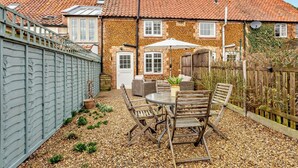 Eine Terrasse mit Tisch und Stühlen, ein kleiner Gartenbereich und eine Steinmauer.