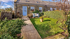 A stone house with a blue door, a small garden, and a pathway leading to the entrance. - 3 Bed in Chathill (oc-62640) (Swinhoe)