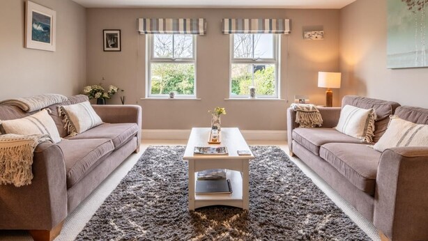 A living room with two sofas, a coffee table, and two windows with striped valances. - 3 Bed in Chathill (oc-62640) (Swinhoe)