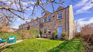 A stone house with a well-maintained lawn and a blue door. - 3 Bed in Chathill (oc-62640) (Swinhoe)
