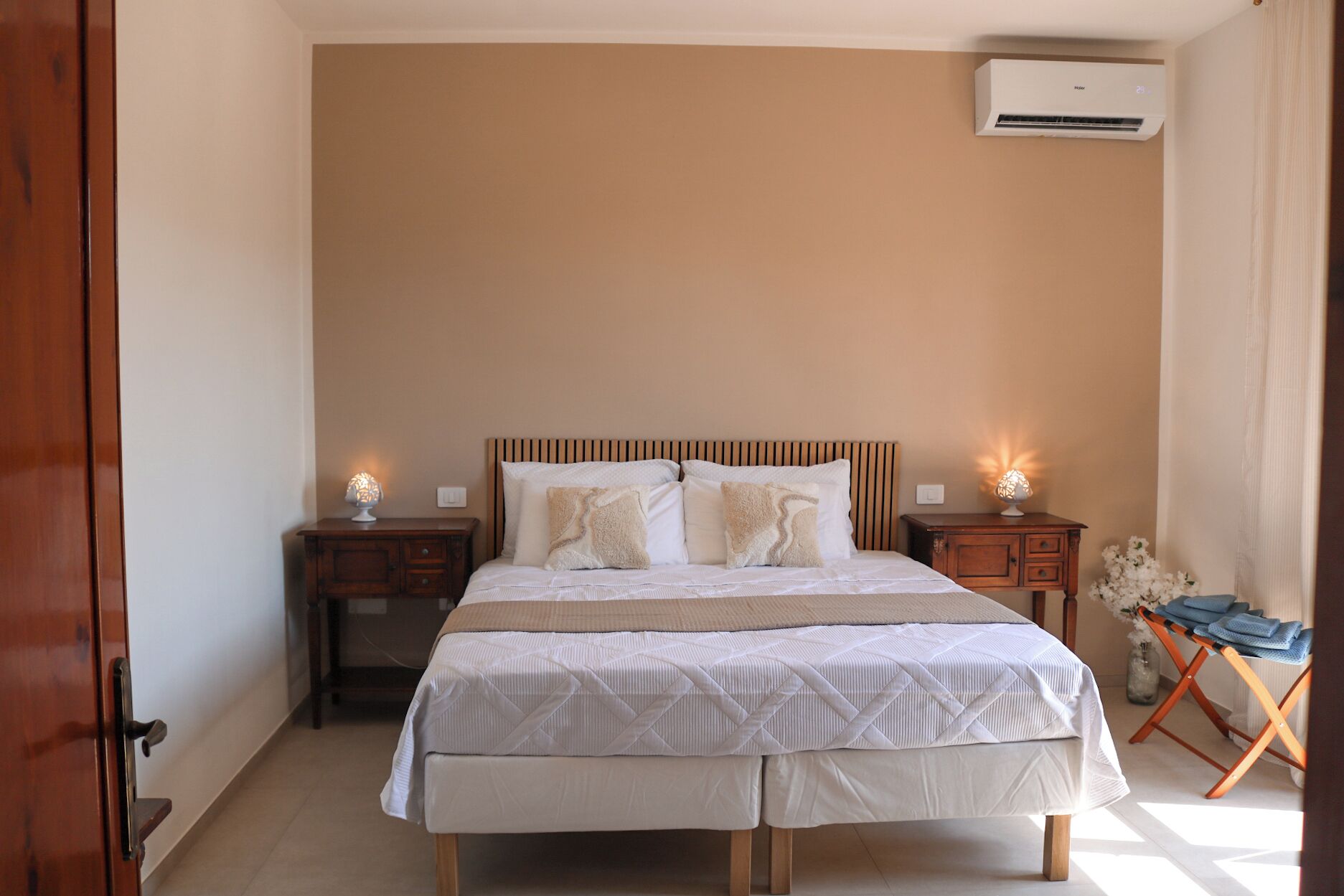 Una camera da letto con un letto, due comodini, un condizionatore d'aria e un tavolino con una lampada.