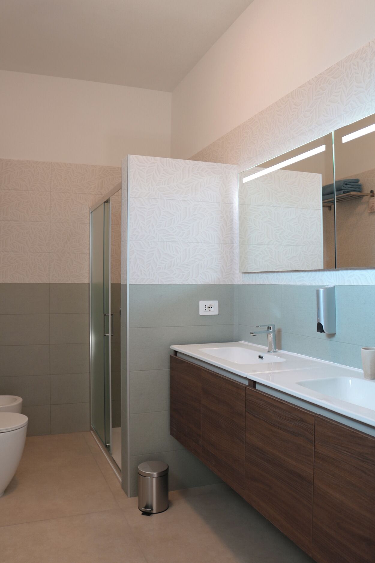 Un bagno moderno con cabina doccia in vetro, un lavandino bianco e un mobile contenitore in legno, e uno specchio grande sopra il mobile.