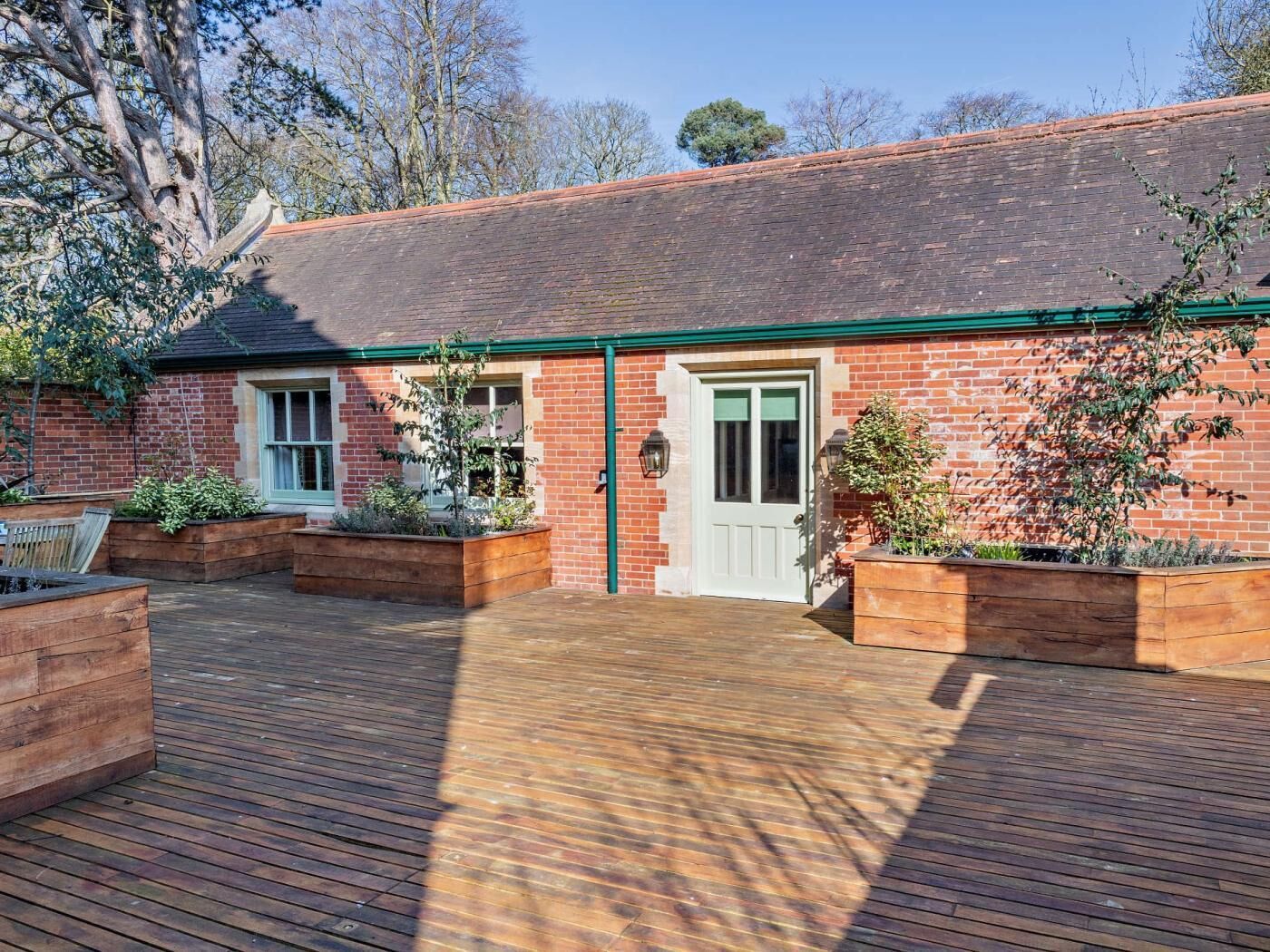 A brick building with a green door and windows, surrounded by wooden decking and raised planters.