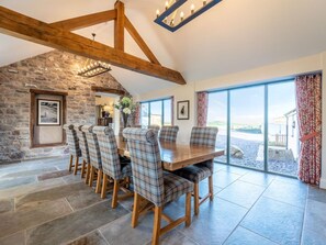 A dining area with a stone wall, wooden beams, and a large table with plaid chairs. - 4 Bed in Denbigh (oc-62947) (Llannefydd)
