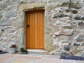 A stone building with a wooden door, a potted plant, and green boots on the steps. - 4 Bed in Denbigh (oc-62947) (Llannefydd)