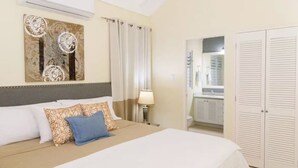 A hotel room with a bed, a nightstand, a lamp, a wardrobe, and a bathroom visible through an open door. - Coolshade - Richmond Estate  (St. Ann Parish)
