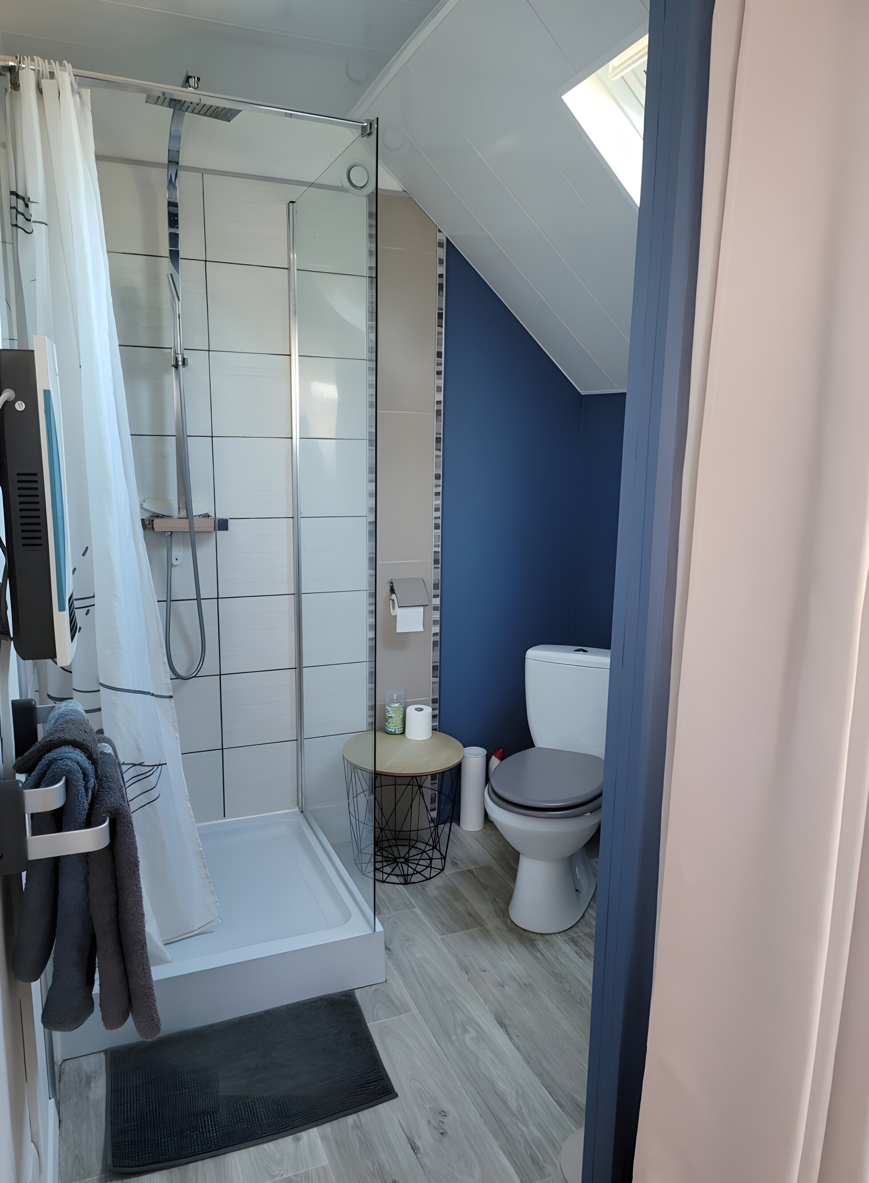 Moderni kylpyhuone, jossa on lasinen suihkuseinä, wc ja pieni pyöreä pöytä, jonka päällä on hygieniatarvikkeita.