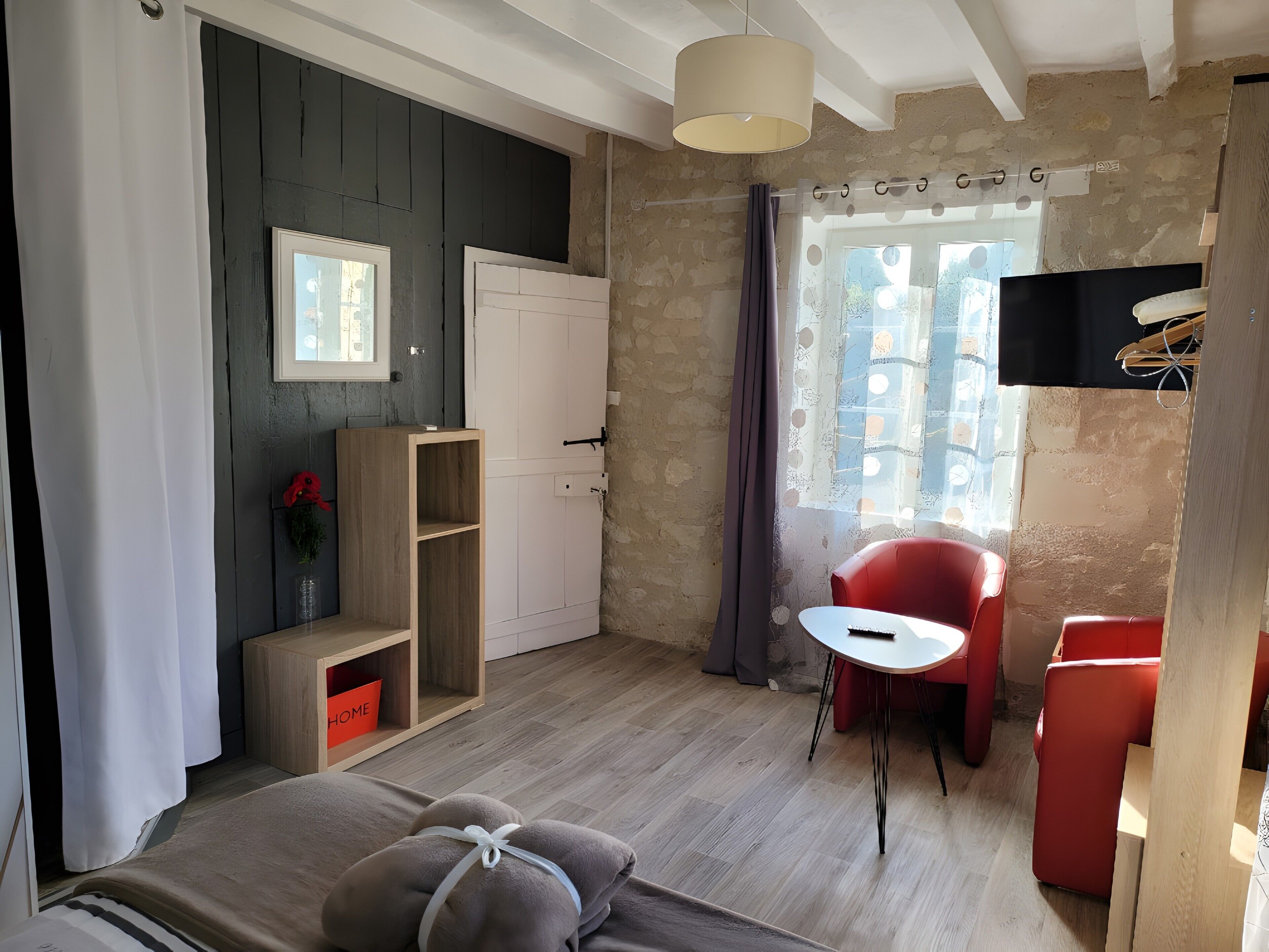A room with a bed, a red chair, a small table, a wooden cabinet, and a TV.