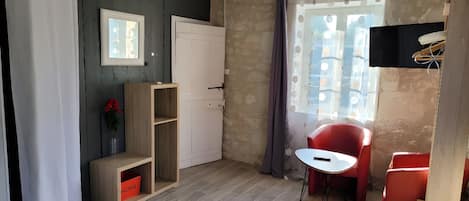A room with a bed, a red chair, a small table, a wooden cabinet, and a TV.