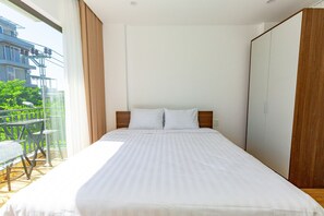 A bedroom with a bed, a wooden wardrobe, and a balcony with a table and chairs. - The BHA Riverside (Da Nang)