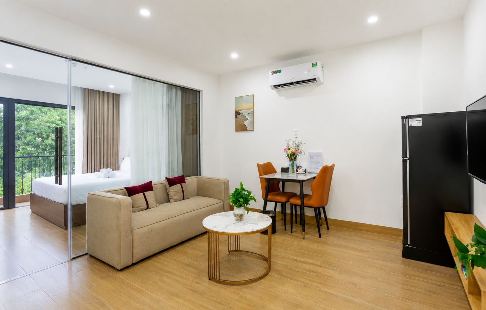 A modern living room with a sofa, a dining table with chairs, a coffee table, an air conditioning unit, and a refrigerator.
