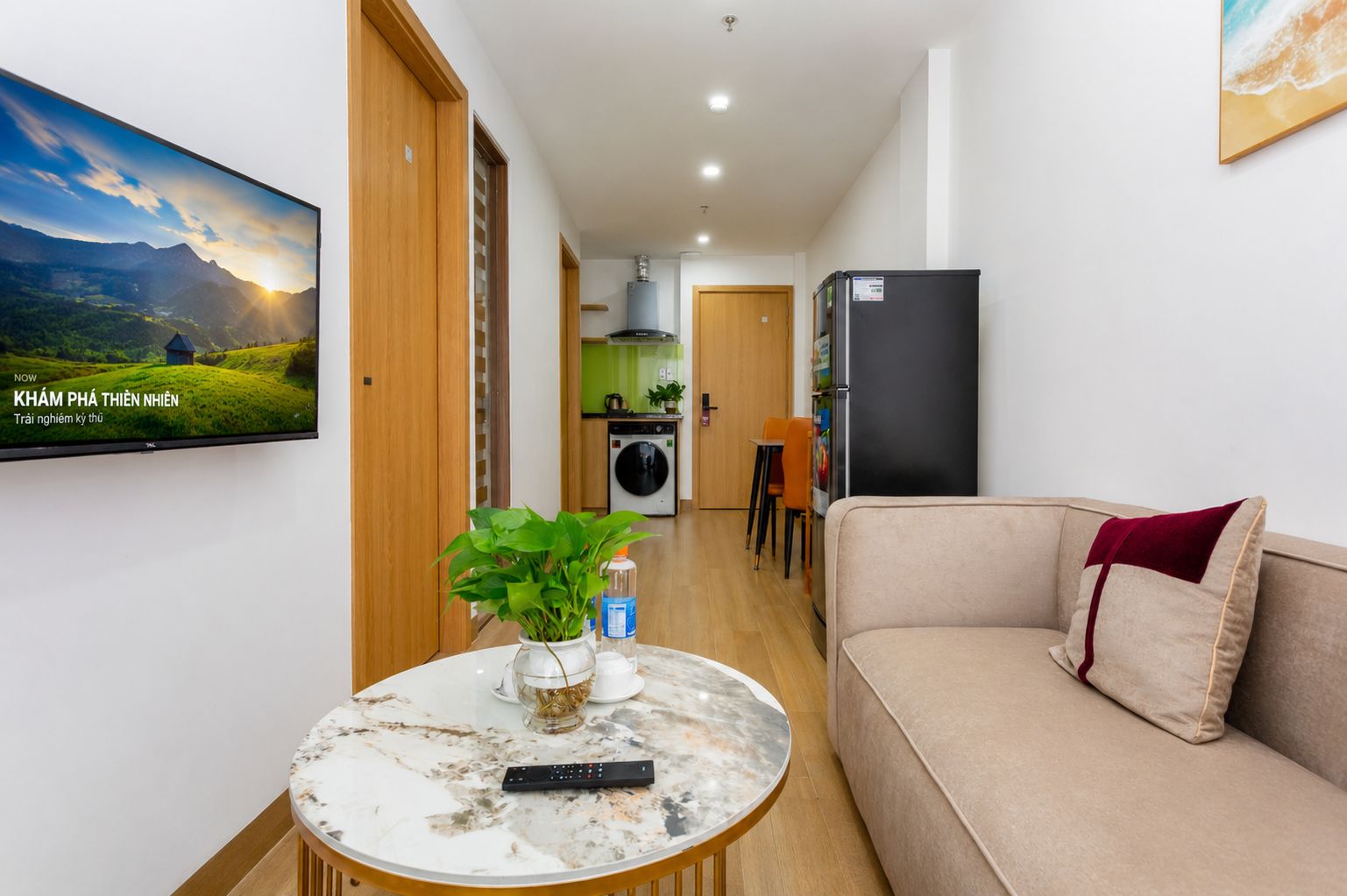 A modern living room with a sofa, a coffee table with a remote control, and a television displaying a scenic landscape.
