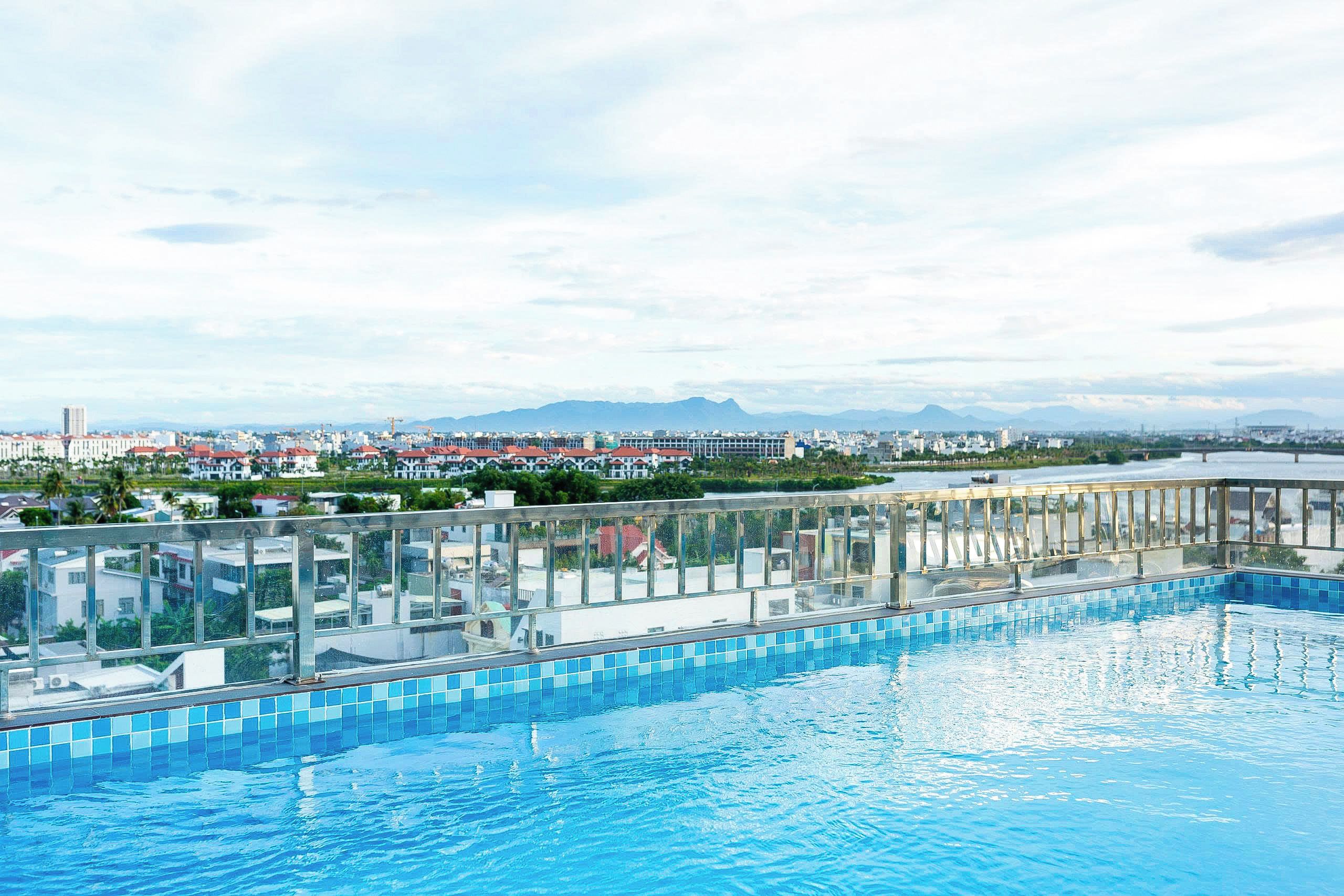 A rooftop swimming pool with a clear view of a cityscape and mountains in the distance.
