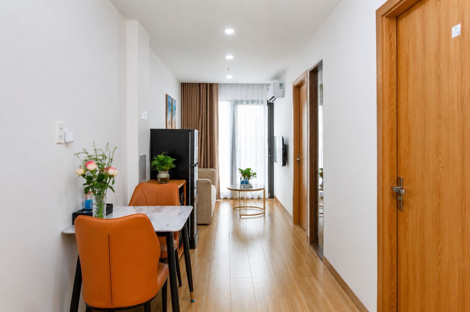 A hotel room with a wooden door, a dining area with a table and chairs, a small sofa, and a potted plant.