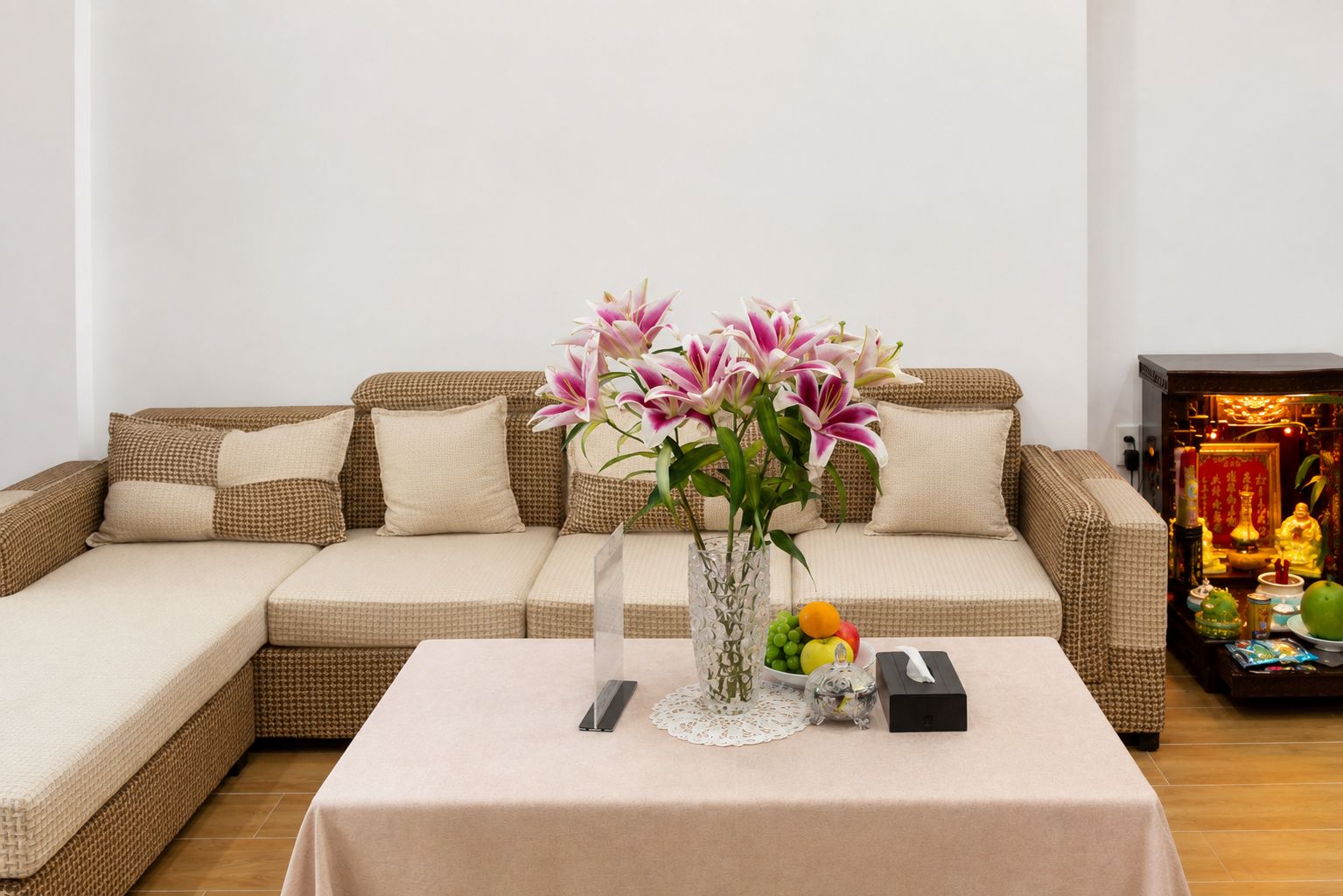 A living room with a sofa, a table with a vase of flowers, and a small shrine.