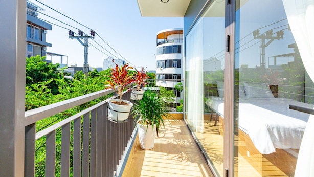 Un balcón con plantas en macetas, una cama y vistas de edificios circundantes.