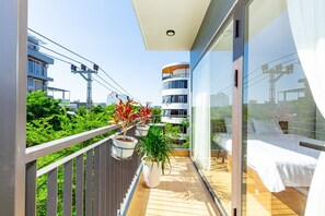 A balcony with potted plants, a bed, and a view of surrounding buildings. - The BHA Riverside (Da Nang)