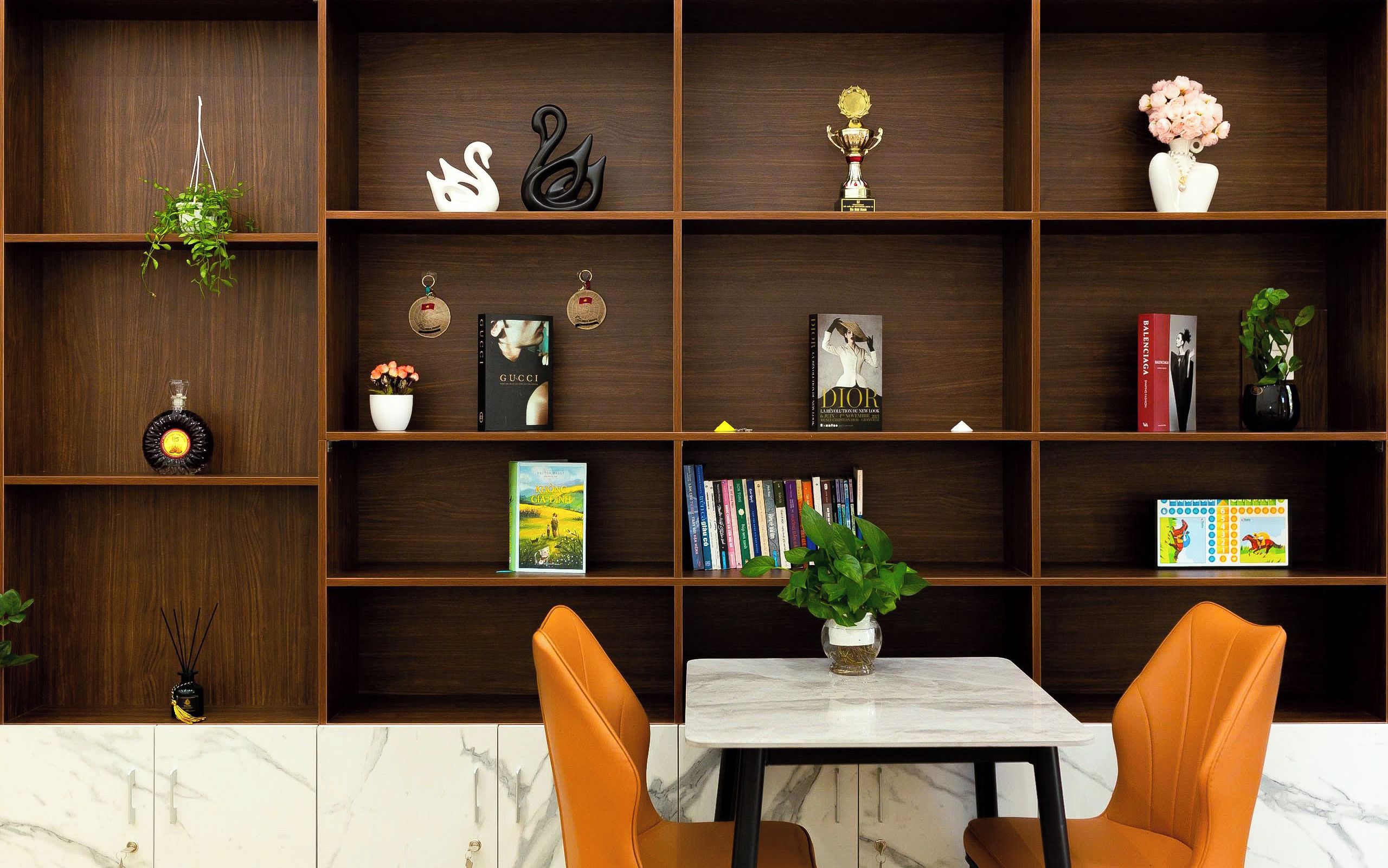 A modern interior with a wooden bookshelf, a marble table, and two orange chairs.