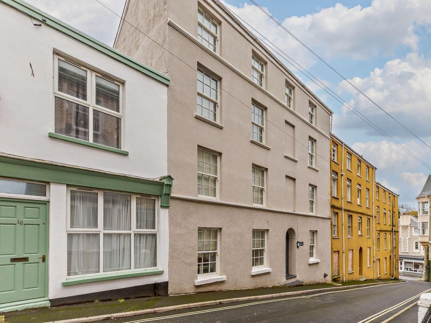 A row of multi-story buildings with distinct architectural styles, including a building with a green door and white trim, and another with a yellow facade.