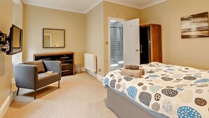 Ein Schlafzimmer mit einem Bett, einem Sessel, einer Kommode, einem Spiegel und einer Dusche.