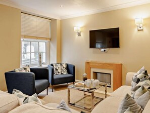 A living room with a fireplace, two armchairs, a sofa, a coffee table, and a TV mounted on the wall. - 5 Bed in Ilfracombe (oc-64914) (Ilfracombe)