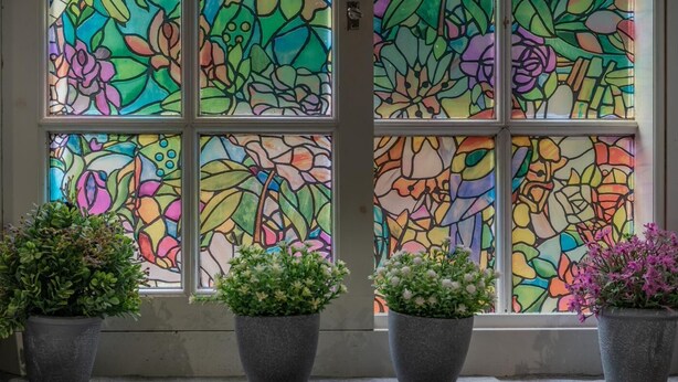 Uma janela com vitrais coloridos e quatro vasos com plantas numa plataforma.