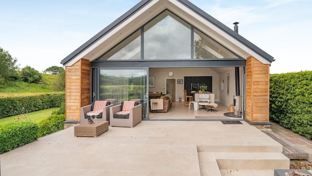 A modern house with a large glass front, a dining area, and a patio with outdoor furniture. - 3 Bed in Blackburn (oc-64911) (Balderstone)