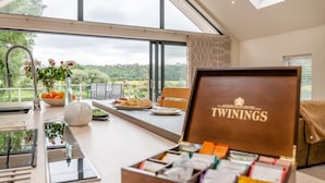 A dining area with a view of the countryside, a table set with food, a vase with flowers, and a box labeled 'TWININGS'. - 3 Bed in Blackburn (oc-64911) (Balderstone)