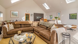 A spacious living area with a large brown sectional sofa, a dining table with chairs, a kitchen in the background, and skylights. - 3 Bed in Blackburn (oc-64911) (Balderstone)