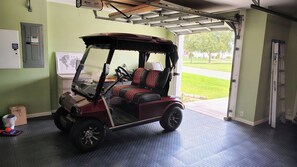 Ein Golfmobil steht in einer Garage mit Metallbedachung und einer Tür zum Freien.