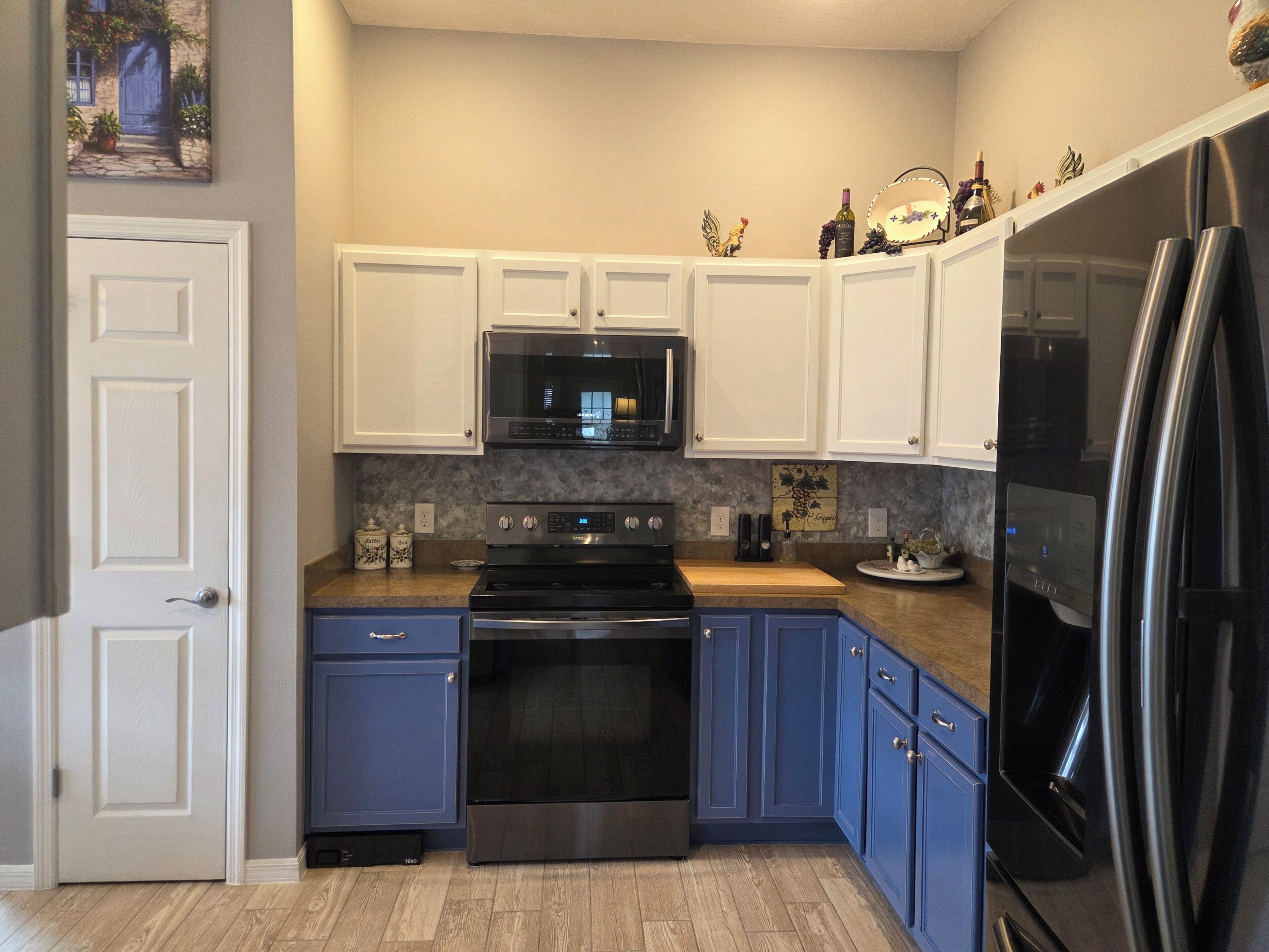 A kitchen with white upper cabinets, a black microwave, stainless steel appliances, and a wooden countertop.