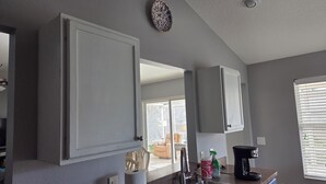 Eine Küche mit grauen Schränken, einer Edelstahl-Spüle, einer Kaffeemaschine und einem Fenster mit Jalousien.