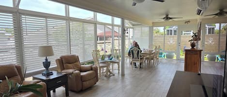 A spacious living area with a large window, ceiling fans, and a dining table with chairs.