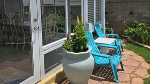 Ein überdachter Patio-Bereich mit Tisch und Stühlen, einem großen Kübelpflanzen und einer Schiebetür.