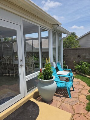 Ein überdachter Patio-Bereich mit Tisch und Stühlen, einem großen Kübelpflanzen und einer Schiebetür.