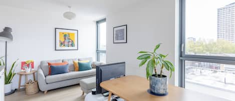 Una sala de estar moderna con un sofá gris, una mesa de comedor de madera, un ventanal grande y una planta en maceta.
