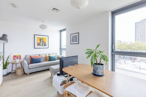 Ein modernes Wohnzimmer mit einem grauen Sofa, einem Holzesstisch, einem großen Fenster und einer Zimmerpflanze.