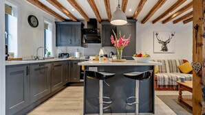 Een moderne keuken met donkere kastjes, een centraal eiland met krukken, een hanglamp en een klok aan de muur.