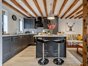 A modern kitchen with dark cabinets, a central island with stools, a hanging light fixture, and a wall-mounted clock. - 3 Bed in Salisbury (oc-66130) (Redlynch)