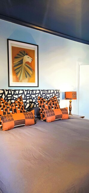 A bed with patterned pillows, a framed artwork on the wall, and a lamp. - Designer Family Home with Garden & Workspace – Walking Distance to the Beach (Cape Town)