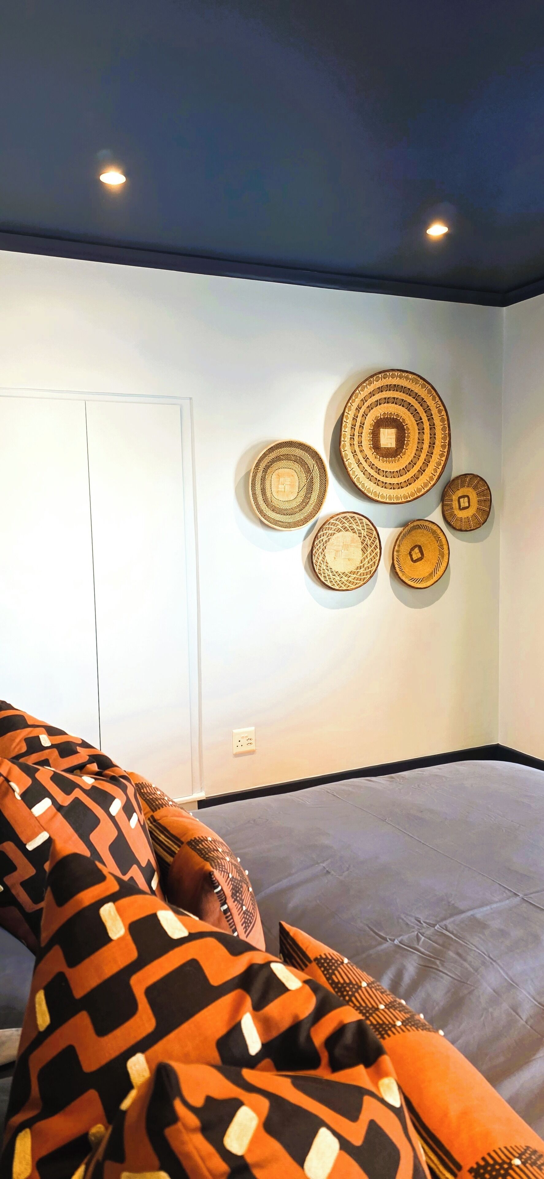 A room with a bed, a wall with circular woven art pieces, and a door.